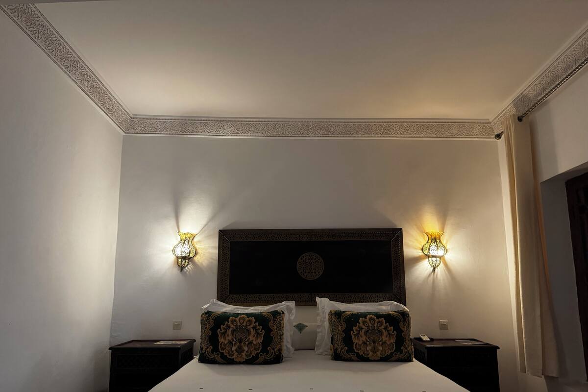 A hotel room with a large bed, two bedside tables, and two wall-mounted lamps.