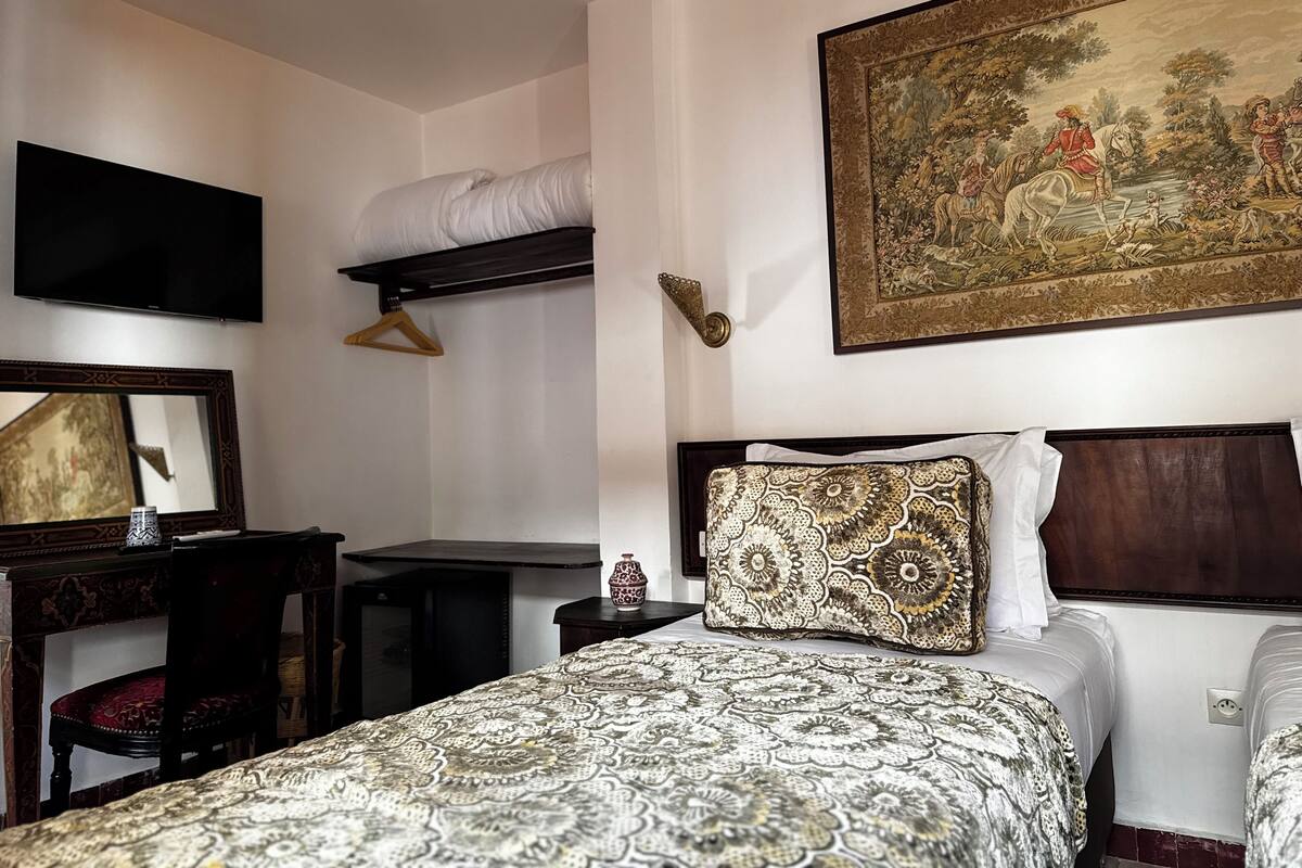 A hotel room with a bed, a television, a painting, and a wardrobe.