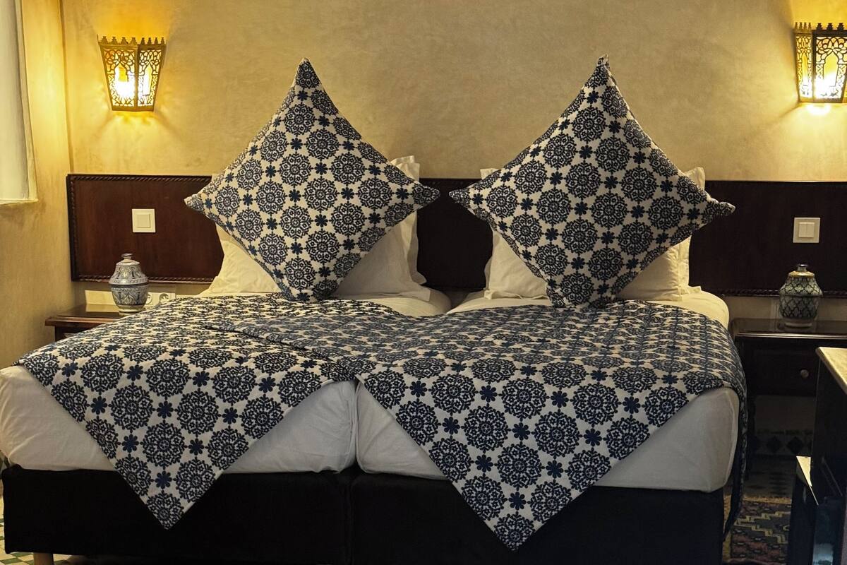 A bed with a patterned bedspread and pillows, a nightstand with a lamp, and a decorative tray on the floor.