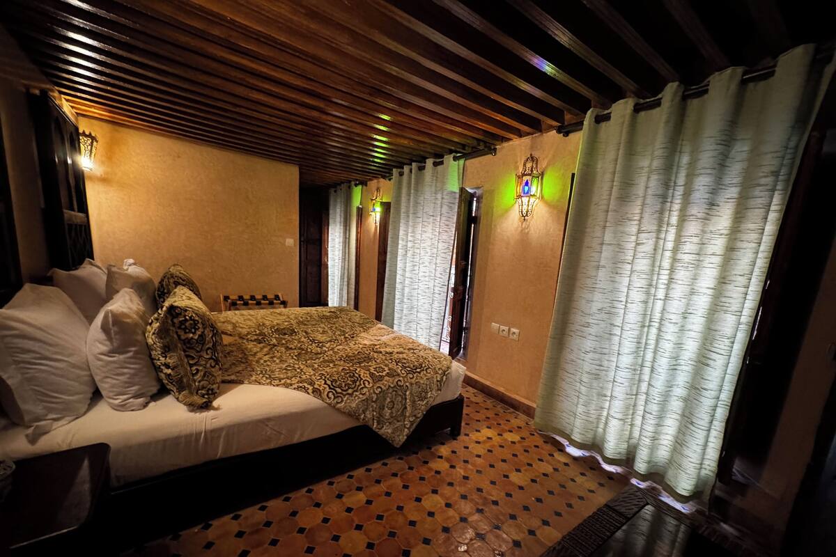 A bedroom with a bed, patterned curtains, and a wooden ceiling.