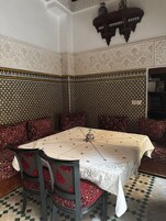 Um quarto com piso xadrez, uma mesa com toalha branca, sofás com padrão vermelho e preto, e desenhos elaborados nas paredes.