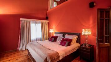 Un dormitorio con una cama grande, dos mesitas de noche con lámparas, un armario de madera y una ventana con cortinas.