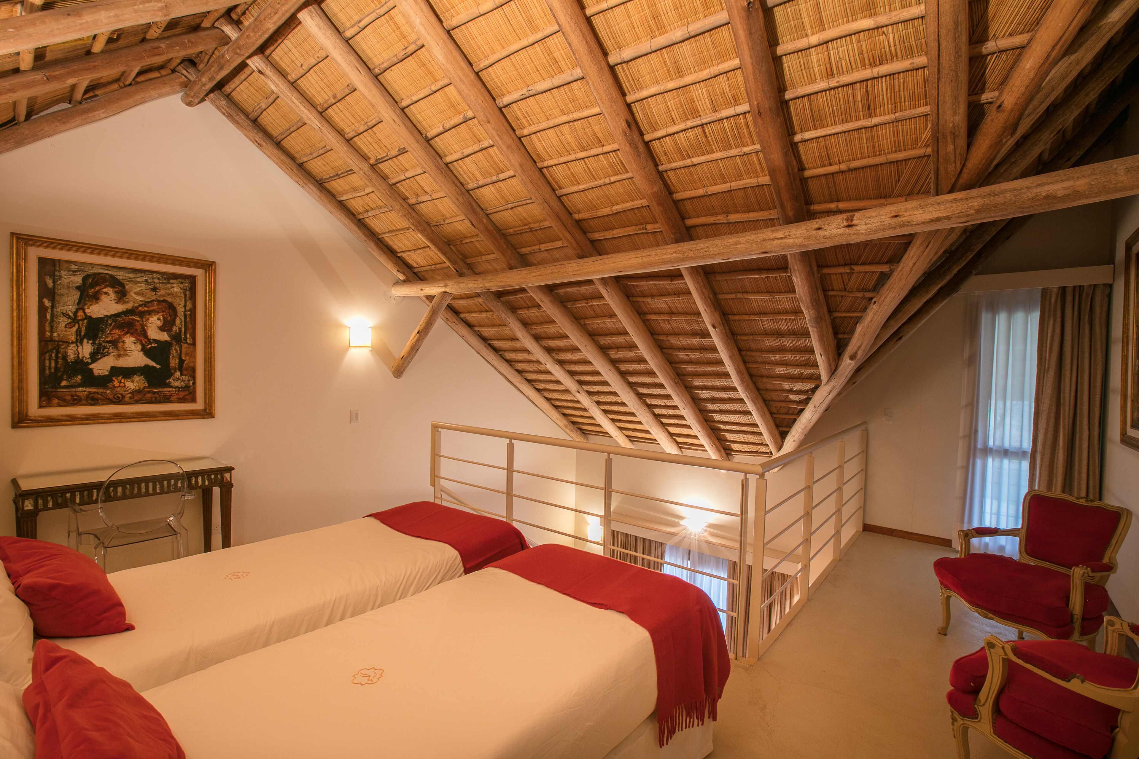 A room with two beds, a wooden ceiling, a painting on the wall, and a chair.