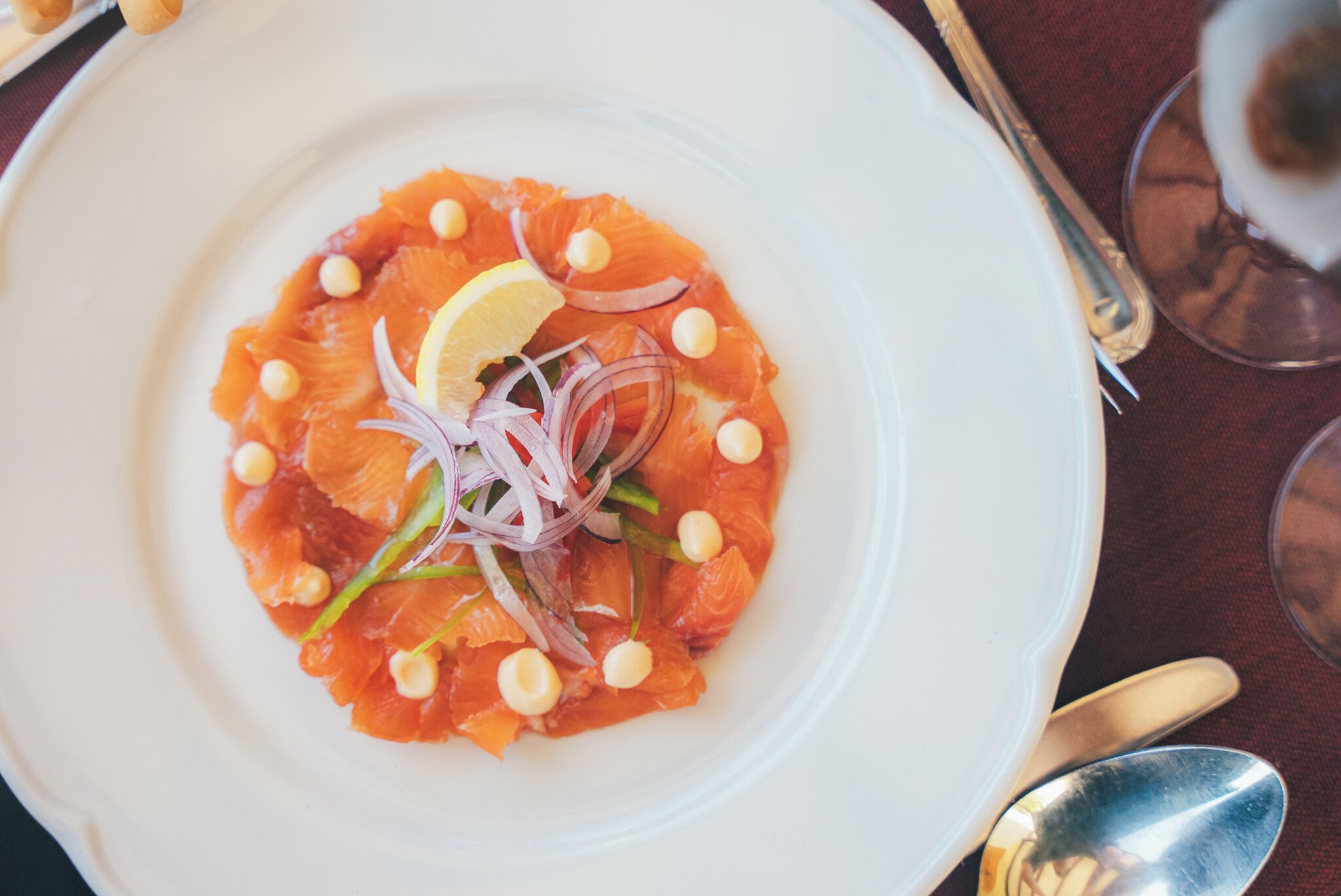 A white plate with a dish of smoked salmon, lemon, and onion garnish.