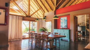 A spacious dining area with a high wooden ceiling, a large window with curtains, and a view of the outdoors.