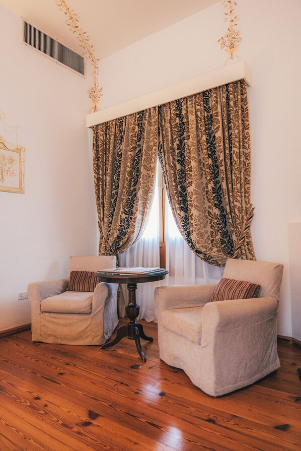 A room with two armchairs, a small round table, and a window with patterned curtains. - Estancia El Colibri - Relais & Châteaux (Ascochinga)