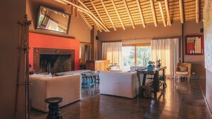 Un salón comedor amplio con techo alto, chimenea y un ventanal con cortinas.