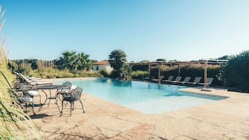 Una piscina al aire libre, sombrillas, sillones reclinables de piscina
