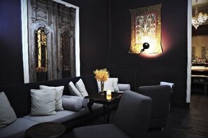 A dark-themed room with a sofa, a small table with a vase of flowers, and a tapestry on the wall. - The Eugenia Hotel & Spa (Bangkok)