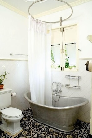 A bathroom with a clawfoot bathtub, a toilet, a window with a view of greenery, and a potted plant. - The Eugenia Hotel & Spa (Bangkok)