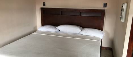 A single bed with a wooden headboard, white bedding, and a light-colored wall.