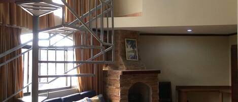 A living room with a blue sofa, a fireplace, and a spiral staircase.