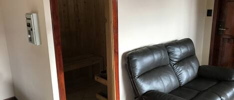 Una habitación con un sofá de cuero negro, un banco de madera y piso de baldosas.