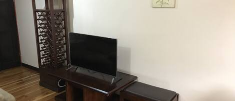 A living room with a wooden entertainment unit, a flat-screen TV, and a small bench.