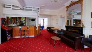 A hotel lobby with a red carpet, a bar area with stools, a black leather sofa, and a large ornate mirror. - Glendevon Hotel (Bournemouth)