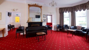 A room with a red carpet, black sofa, and multiple chairs. - Glendevon Hotel (Bournemouth)
