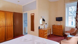 A hotel room with a large bed, wooden wardrobe, a dresser, a television, and a window with a view of buildings. - Glendevon Hotel (Bournemouth)