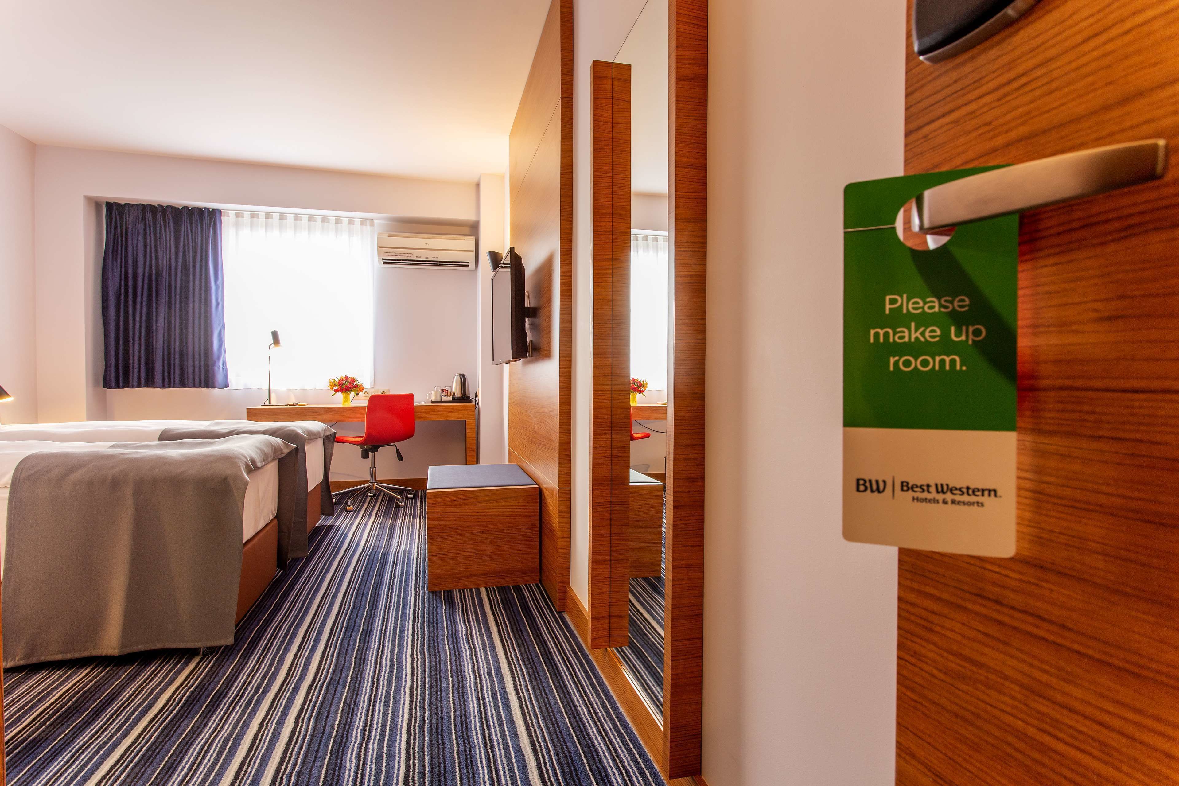 Habitación de hotel con cama, escritorio, silla y un cartel que dice 'Por favor, hacer la cama'.