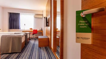 Habitación de hotel con cama, escritorio, silla y un cartel que dice 'Por favor, hacer la cama'.
