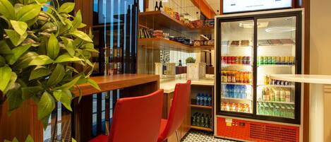A modern bar area with red chairs, a refrigerator stocked with beverages, and a menu display above the bar.