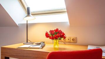 Un bureau avec une lampe, un vase de fleurs rouges et une chaise rouge.
