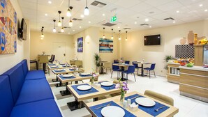 A modern dining area with blue seating, tables set with plates and cutlery, and a kitchen counter with fresh produce. - Best Western Terminus Hotel (Sofia)