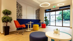 A modern interior with a blue sofa, orange and yellow ottomans, a round table with a vase, and a bookshelf. - Best Western Terminus Hotel (Sofia)
