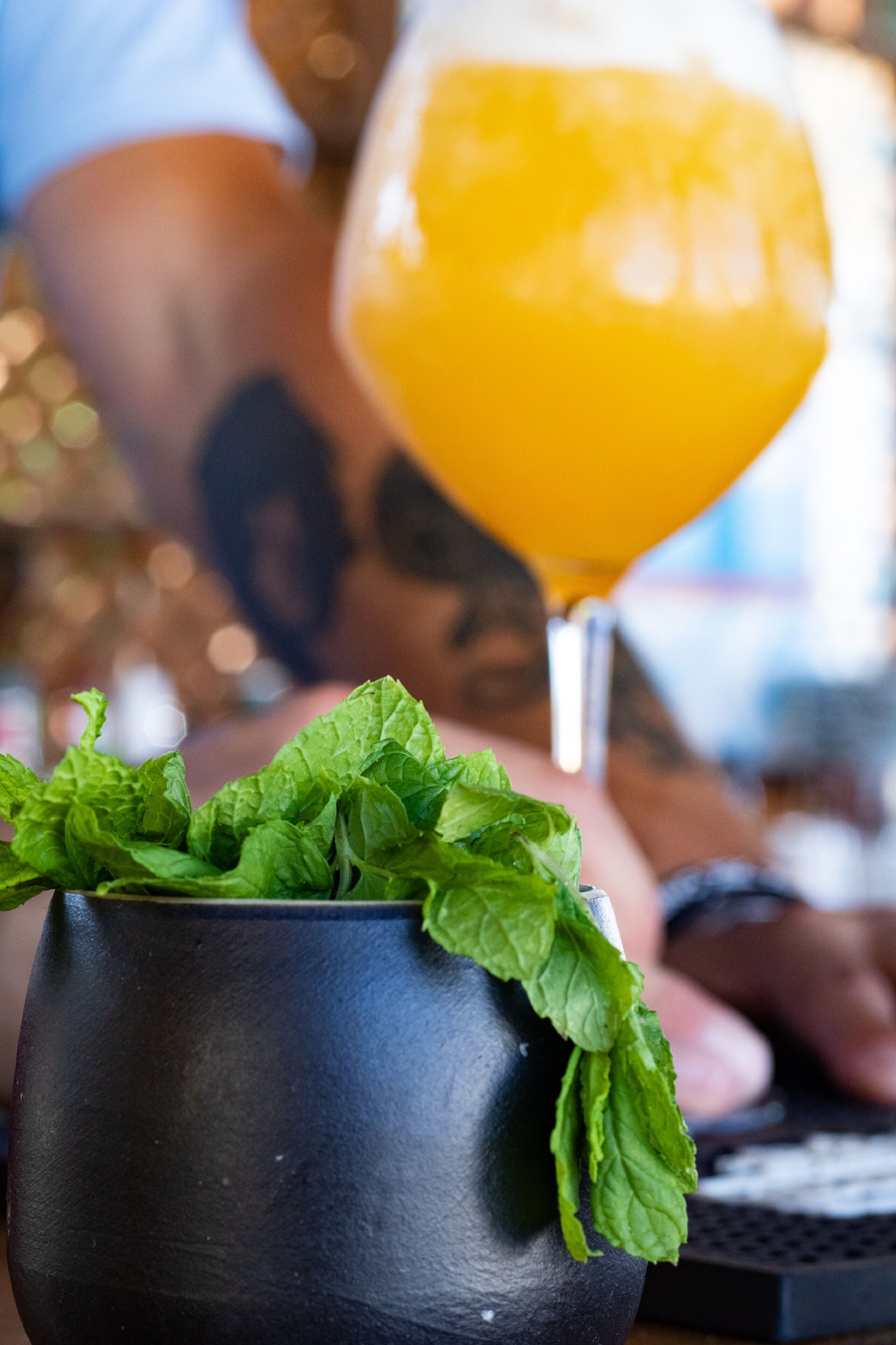 A close-up of a black mug with fresh mint leaves on top, placed on a table.