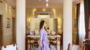 A woman walking through a room with a large round table, chairs, a chandelier, and a mirror.