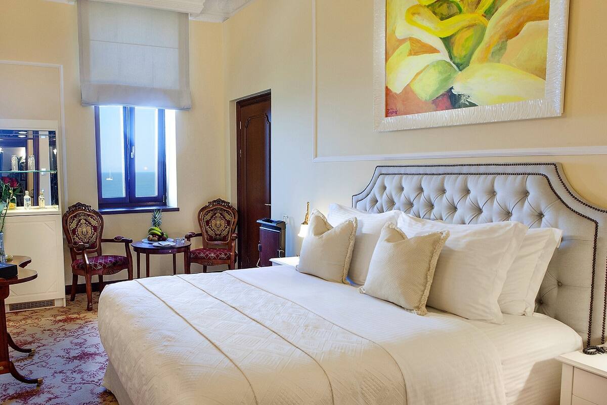 A bedroom with a large bed, a window with a view, and a painting on the wall.