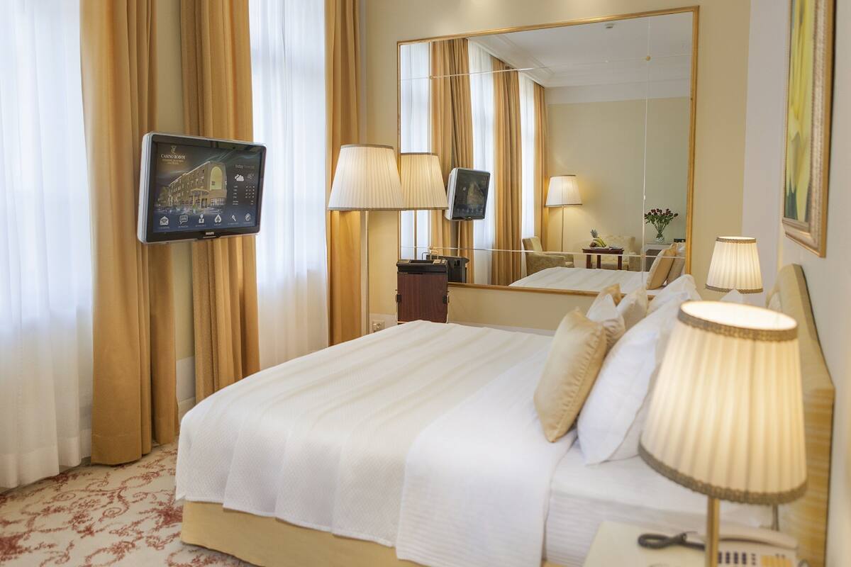 A hotel room with a large bed, a television mounted on the wall, and a mirror reflecting the room.