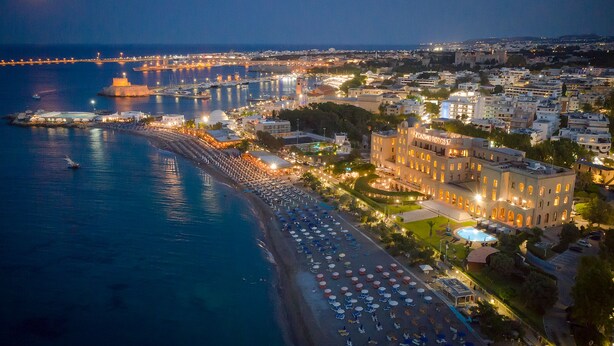 A coastal hotel with a beachside location, a marina, and a prominent building with illuminated windows. - Grande Albergo delle Rose (Rhodes)