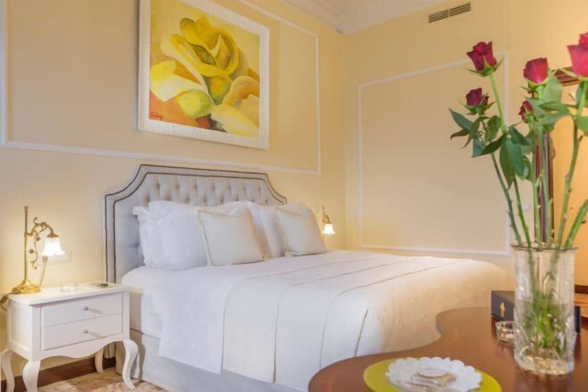 A neatly arranged bedroom with a bed, bedside table, lamp, and a vase with flowers.