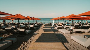 A beach with rows of sun loungers and orange umbrellas, a wooden walkway leading to the water, and a clear view of the sea. - Grande Albergo delle Rose (Rhodes)