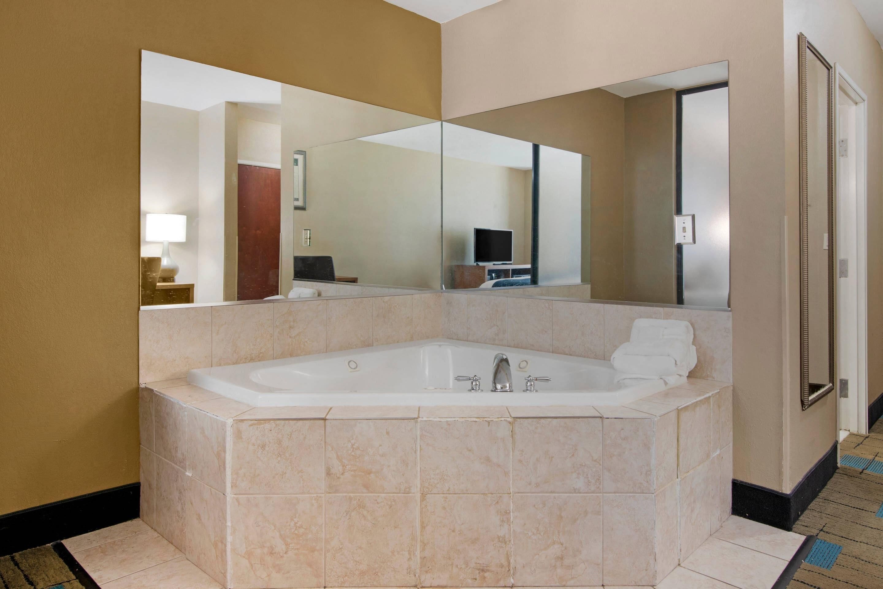 A modern bathroom with a large bathtub, a mirror, and a television in the background.