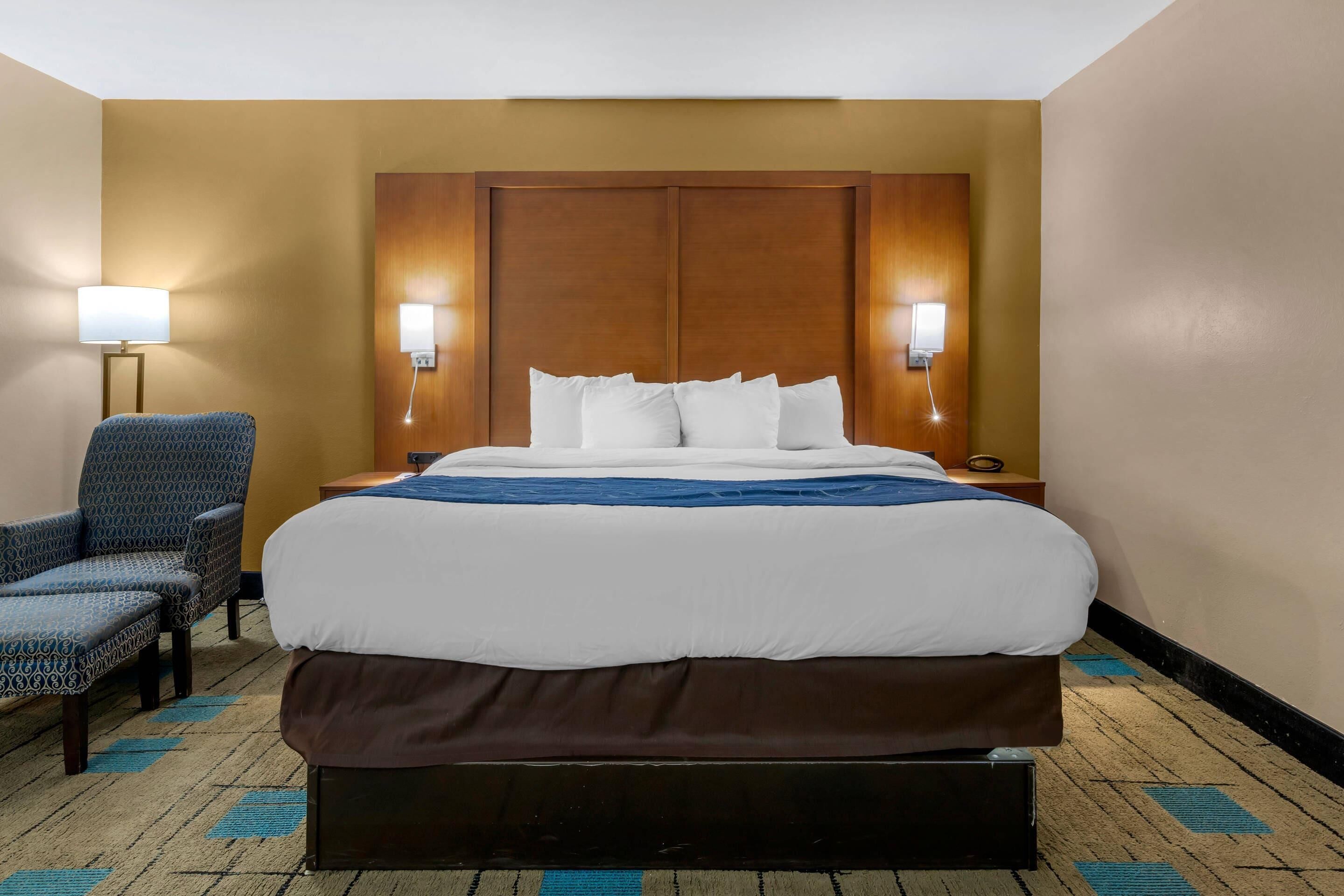 Ein Hotelzimmer mit einem großen Bett, zwei Nachttischlampen, einem Sessel und Teppichboden.