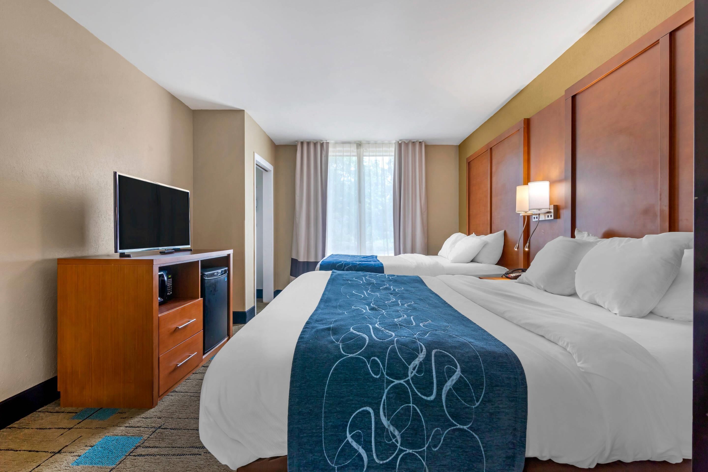 A hotel room with a bed, a TV, a desk with a phone, and a window with curtains.