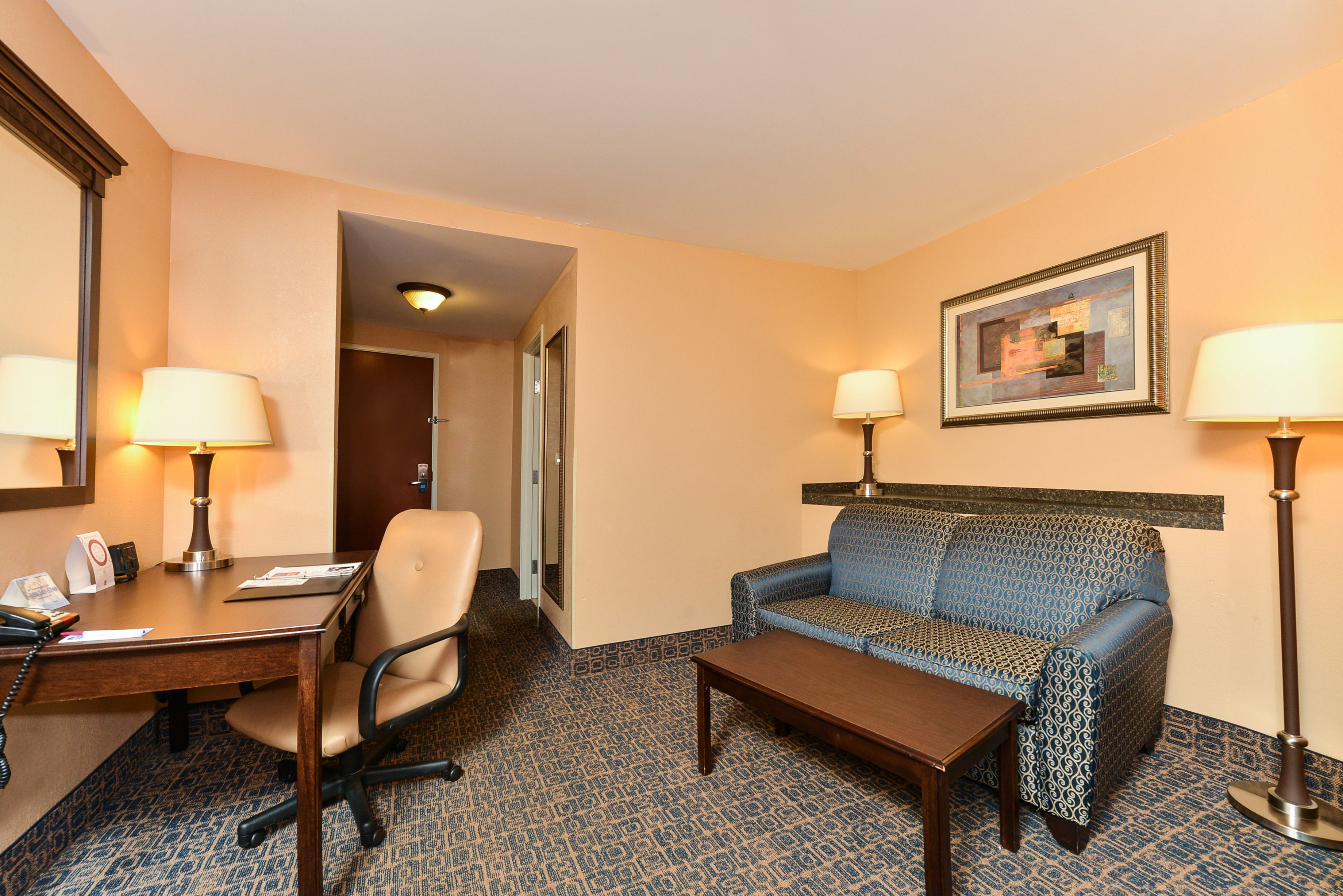 Una habitación de hotel con escritorio, silla, sofá y dos lámparas.