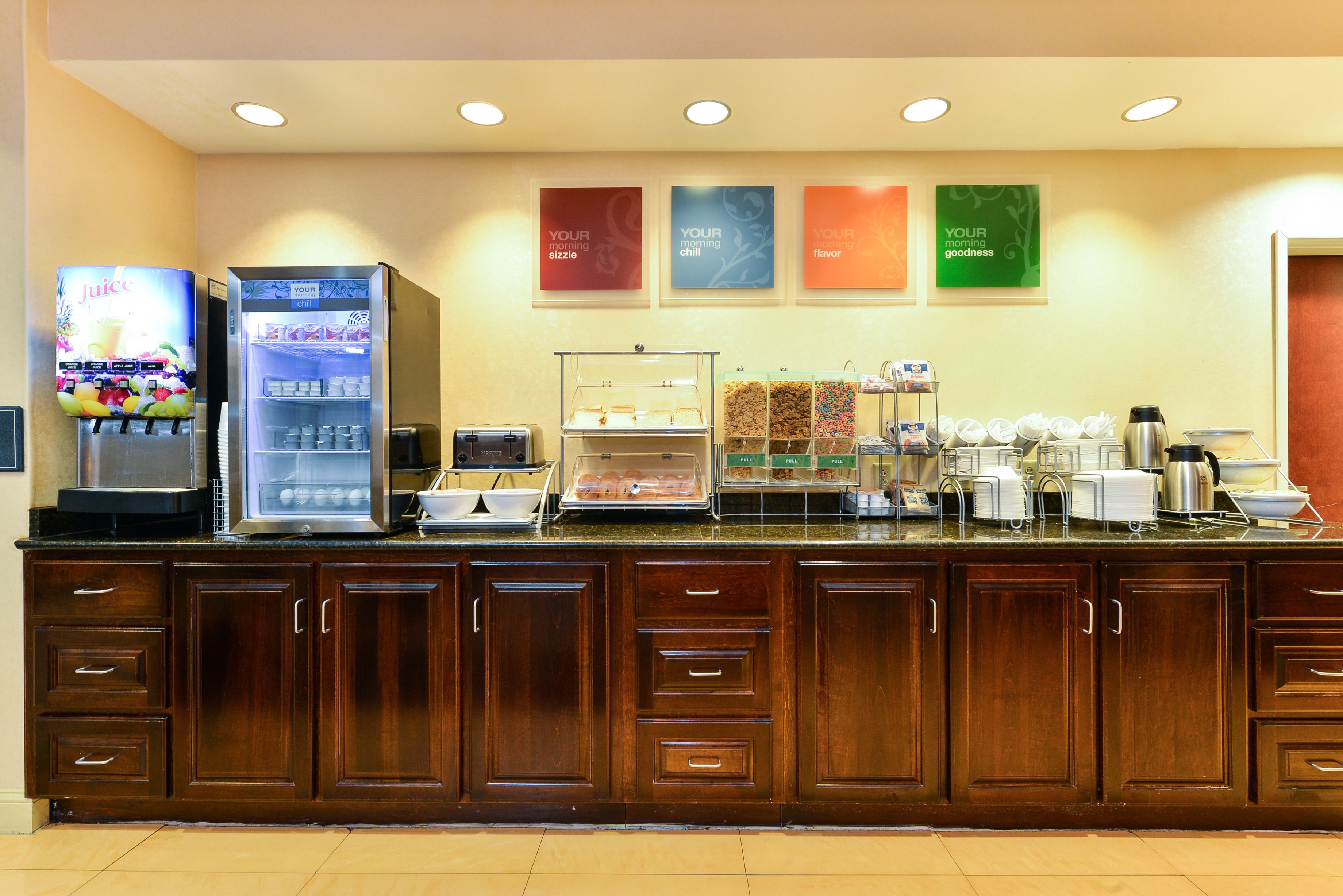 Un área de desayuno de hotel con mostrador, dispensadores de bebidas y una estación de café.