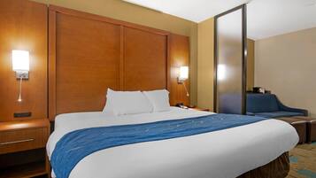 Een hotelkamer met een groot bed, nachtkastjes, een bureau, een stoel en een spiegel.