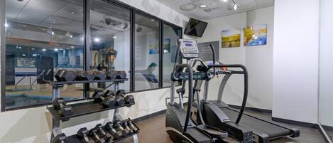 Une salle de sport équipée de matériel d’exercice, d’un tapis de course et d’un mur recouvert de miroirs.