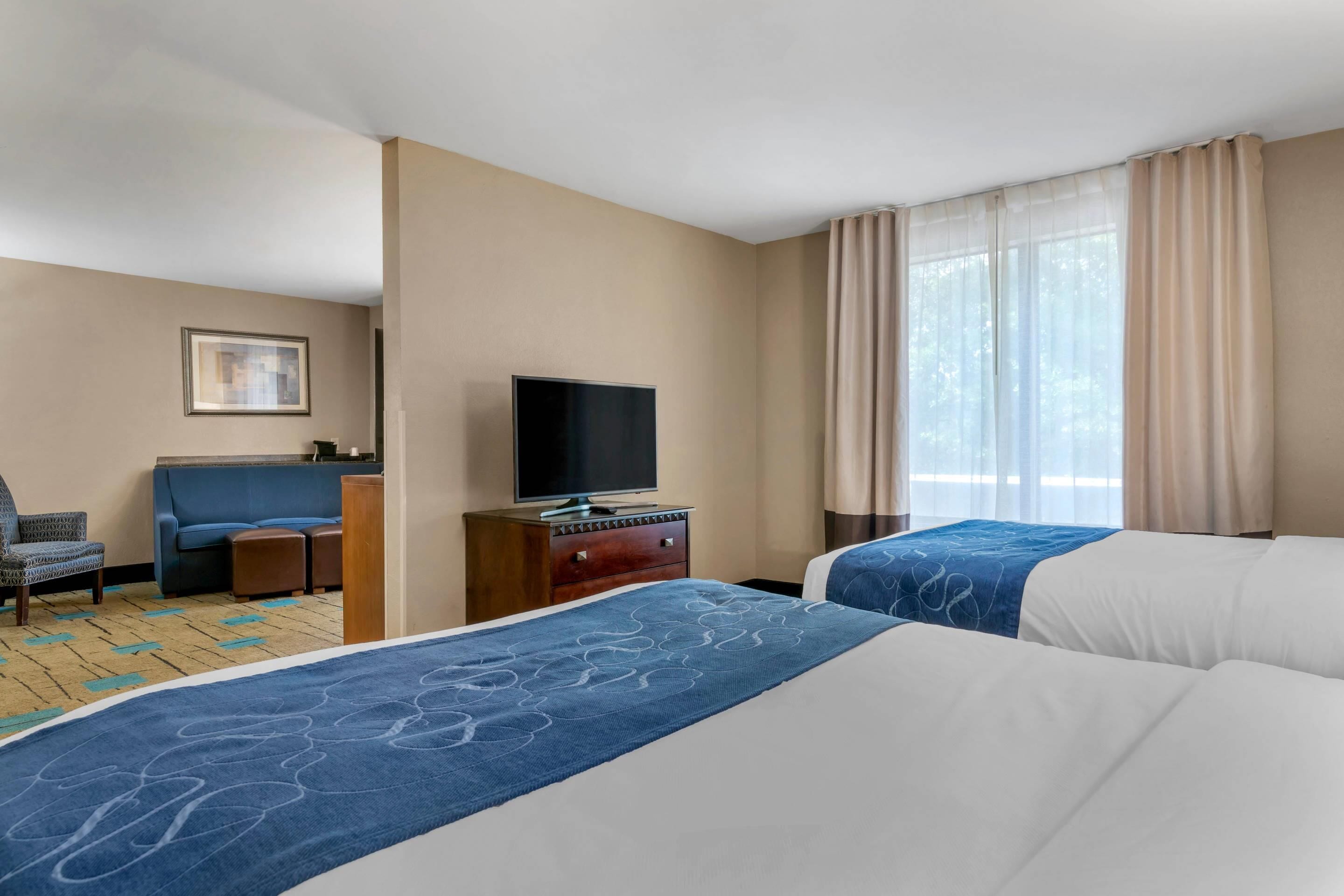 A hotel room with two beds, a TV, a sofa, and a desk.