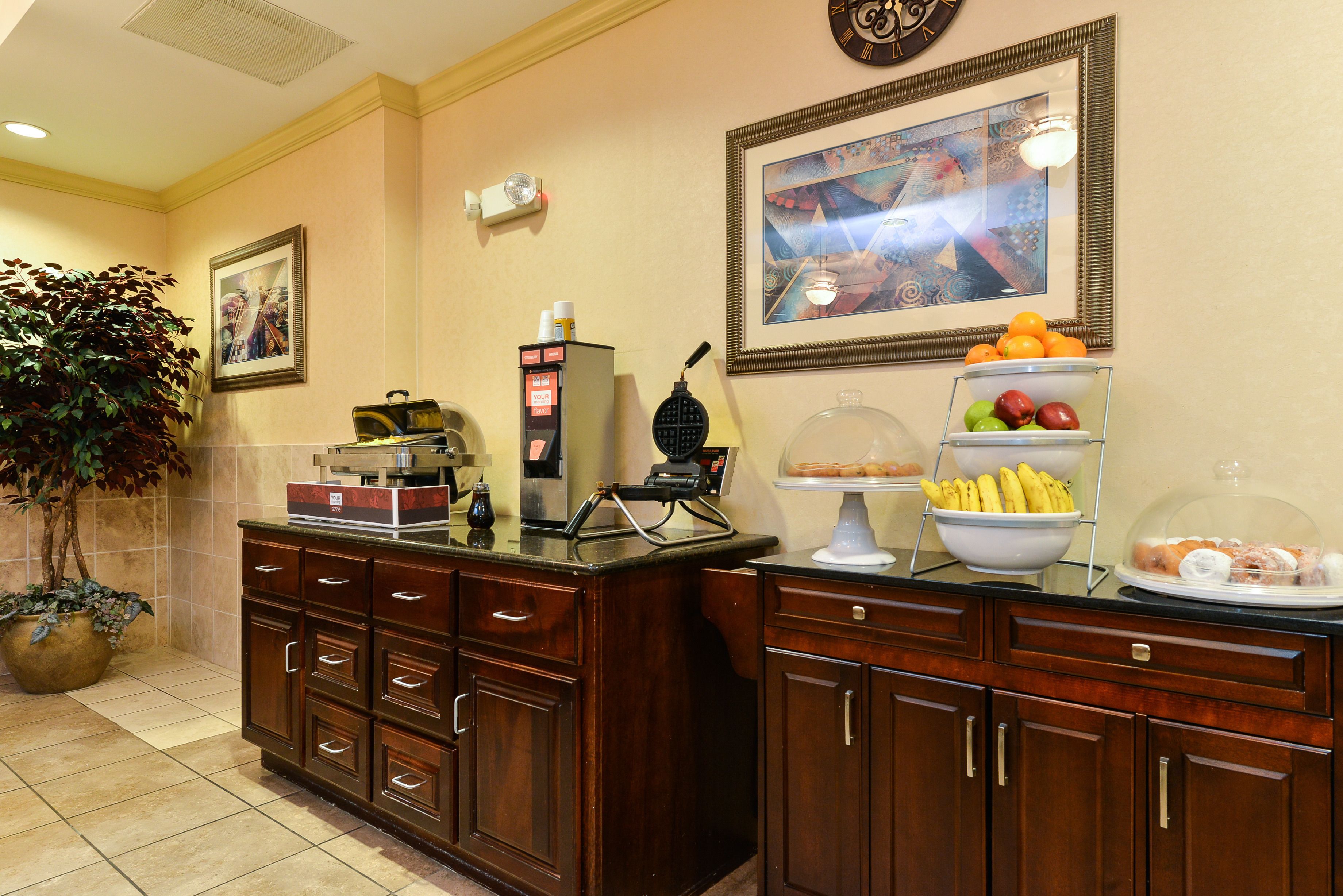 Un'area della reception di un hotel con una macchina per caffè, una ciotola di frutta e un quadro appeso al muro.