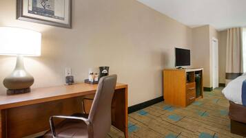 A hotel room with a wooden desk, a chair, a television, a bed, and a carpeted floor.