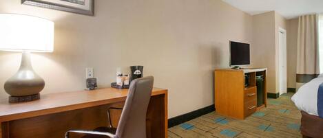 A hotel room with a wooden desk, a chair, a television, a bed, and a carpeted floor.