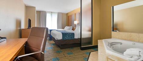 A hotel room with a bed, a desk, a chair, a large mirror, a bathtub, and a television.