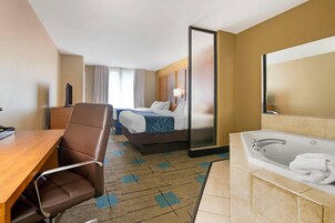 Habitación de hotel con cama, escritorio, silla, espejo grande, bañera y televisor.
