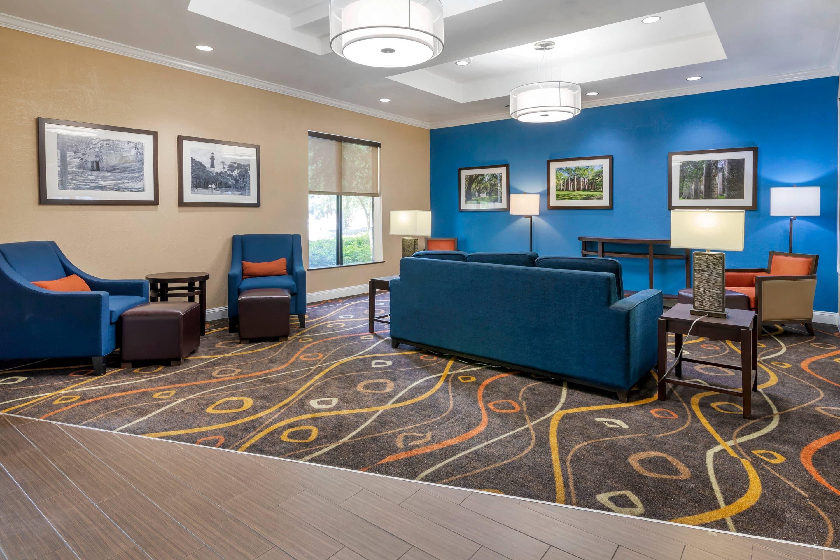 A hotel lobby with a blue sofa, armchairs, a patterned carpet, and framed pictures on the walls.