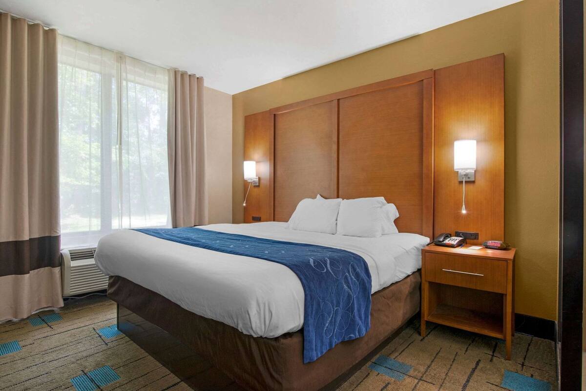 Habitación de hotel con una cama grande, mesitas de noche, un escritorio y una ventana con cortinas.