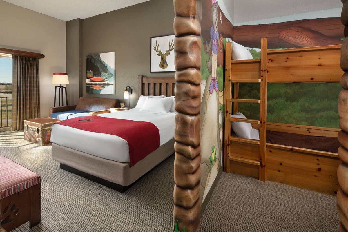 Ein Hotelzimmer mit einem Bett, einem Schreibtisch, einer Lampe, einem Gemälde und einem Stockbett.